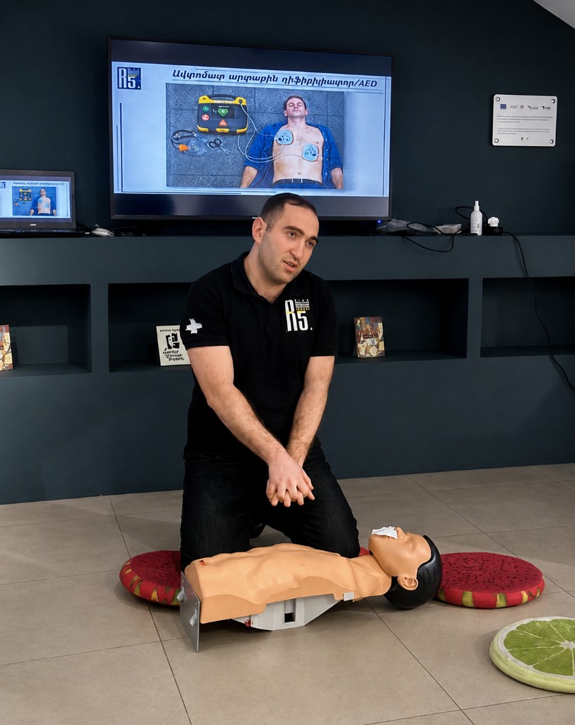 Instructor demonstrating CPR on a mannequin with AED training presentation on screen