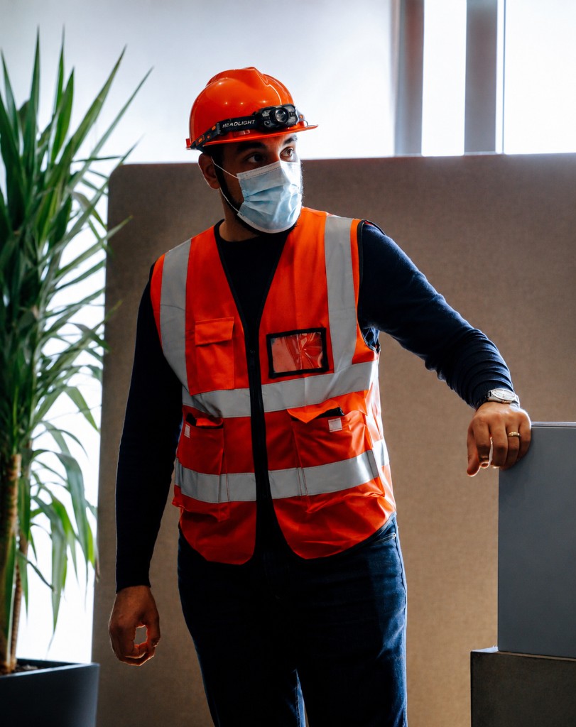 Worker wearing orange hard hat, face mask, and high-visibility safety vest